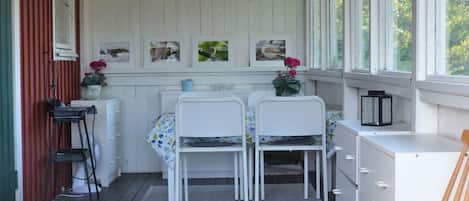 A covered porch with a wooden floor, white furniture, and framed pictures on the wall.
