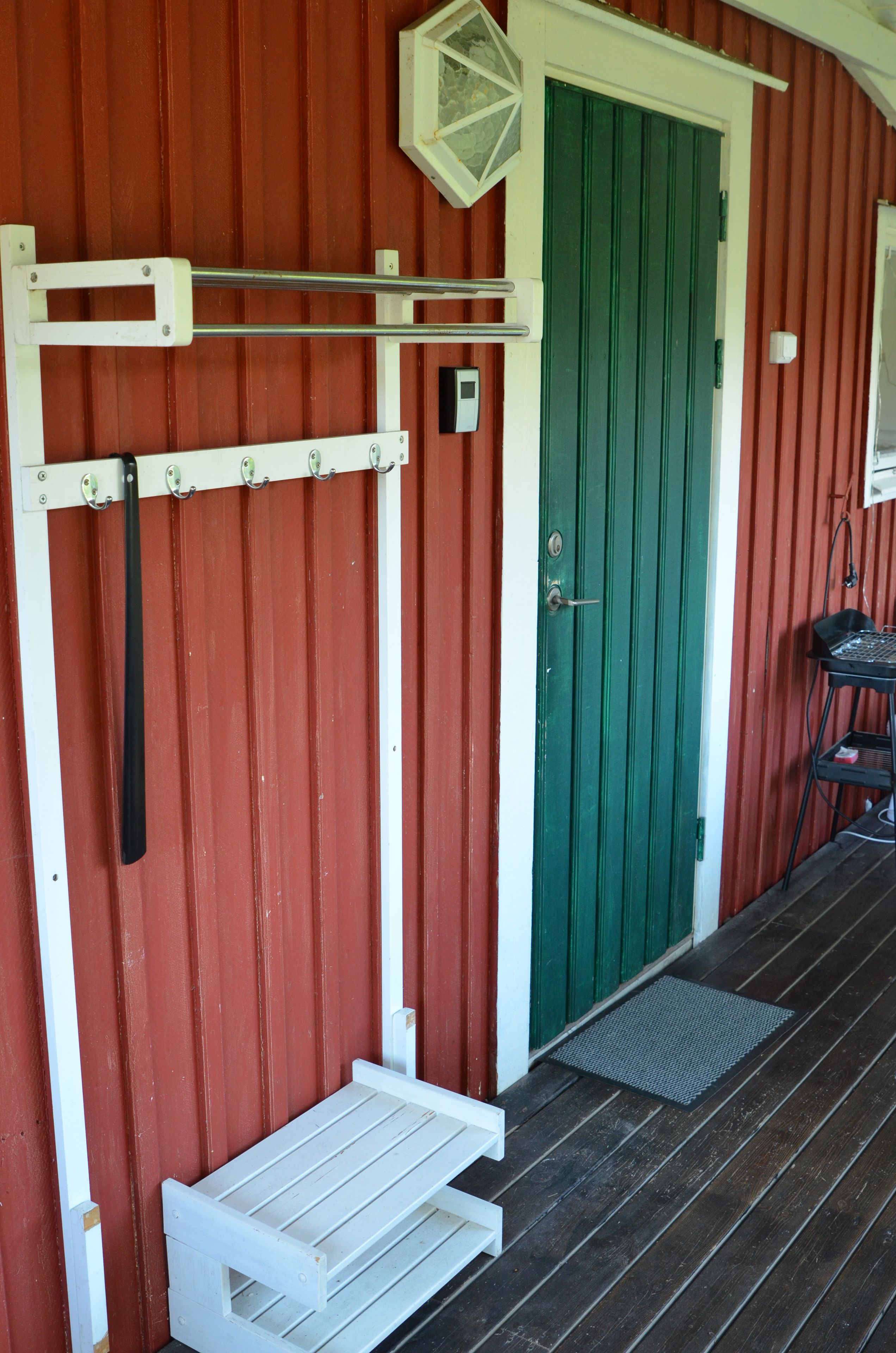 A red building with a green door, a white bench, and a small table.