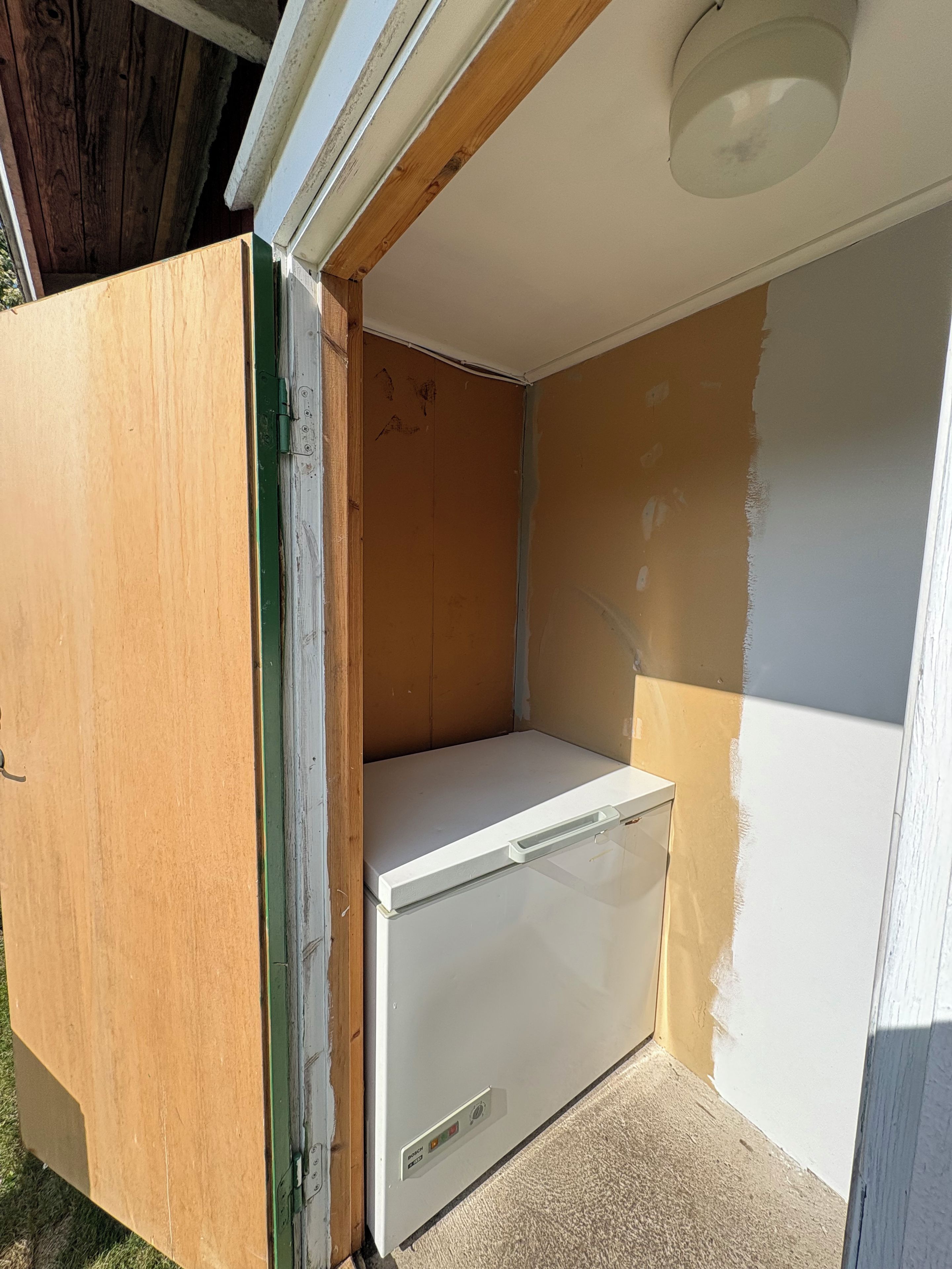 Una habitación con un refrigerador blanco, una puerta de madera y una pared pintada a medias.