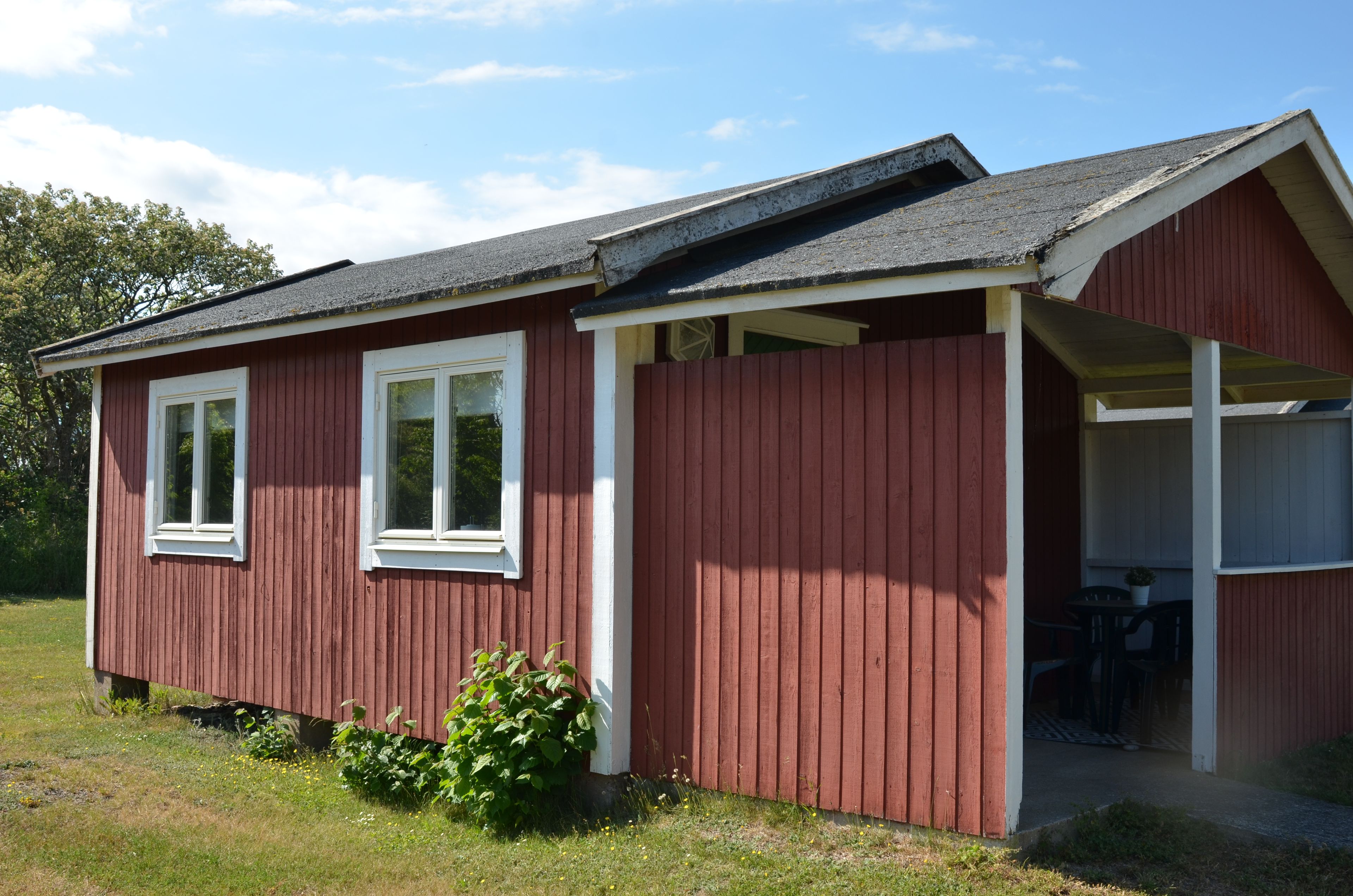 A red wooden building with two windows and a covered porch.