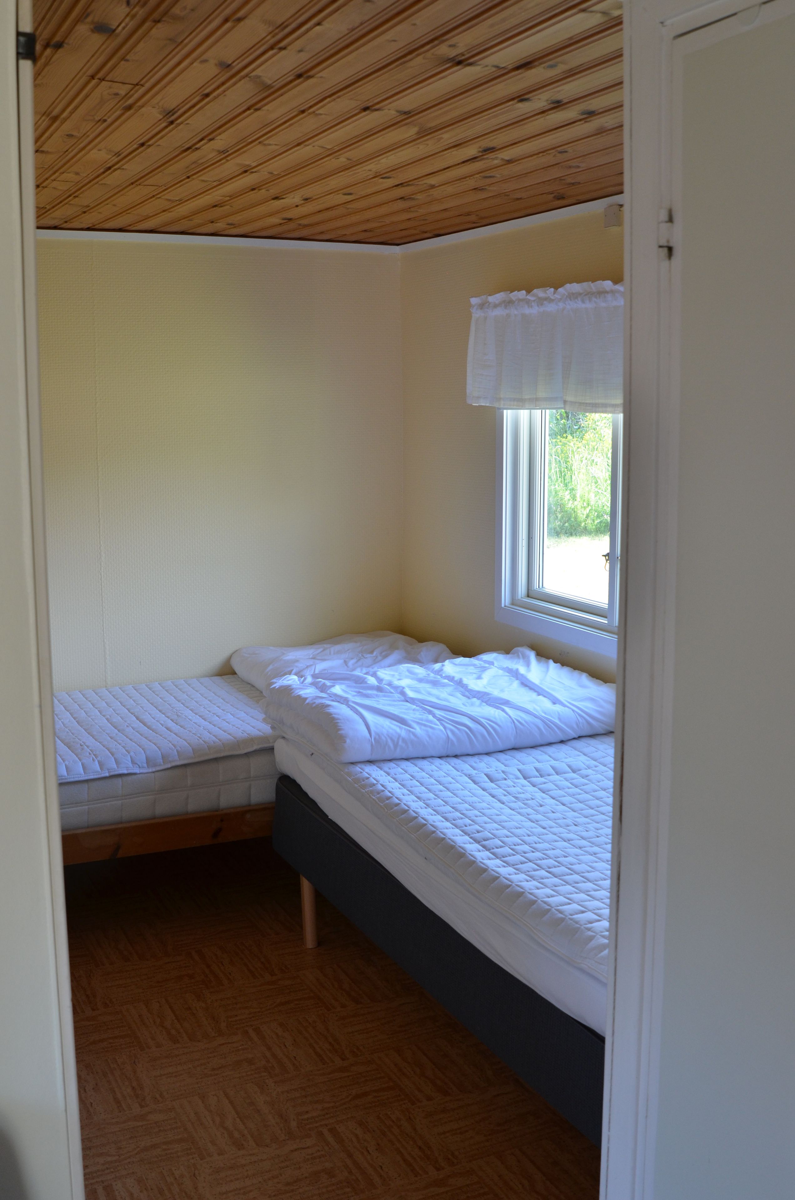 A small, single-bed room with a wooden ceiling and a window.