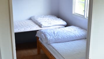 A small, single-room accommodation with two beds, a window with a white curtain, and a wooden floor.