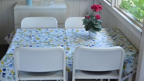 A dining area with a table set for two, white chairs, a floral tablecloth, and a vase with flowers. - Grönhögens Stugby (Degerhamn)