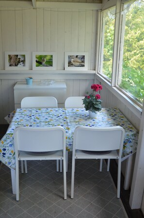 A dining area with a table set for two, white chairs, a floral tablecloth, and a vase with flowers. - Grönhögens Stugby (Degerhamn)