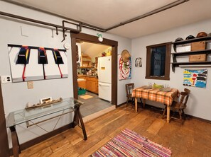 Une cuisine avec une table en bois, des chaises et un réfrigérateur. Il y a une fenêtre donnant sur l’extérieur.