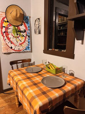 Ein Essbereich mit kariertem Tischläufer, zwei Tellern, einem Glas, einer Obstschale und einer Wand mit einem Gemälde und einem gerahmten Bild.