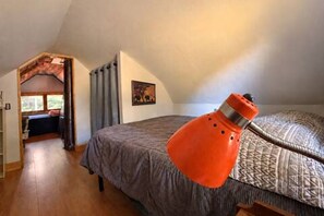 Une chambre avec un plafond en pente, un lit avec une literie à motifs et une lampe orange vif.
