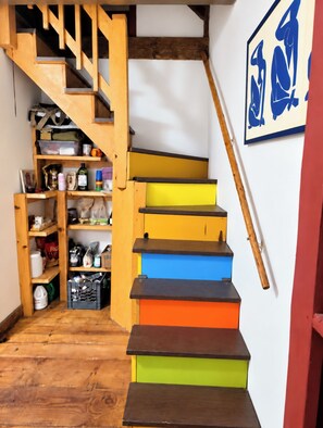 Un escalier en bois à plusieurs niveaux, doté d’une rampe, qui mène à un espace de rangement équipé d’étagères et de bacs.