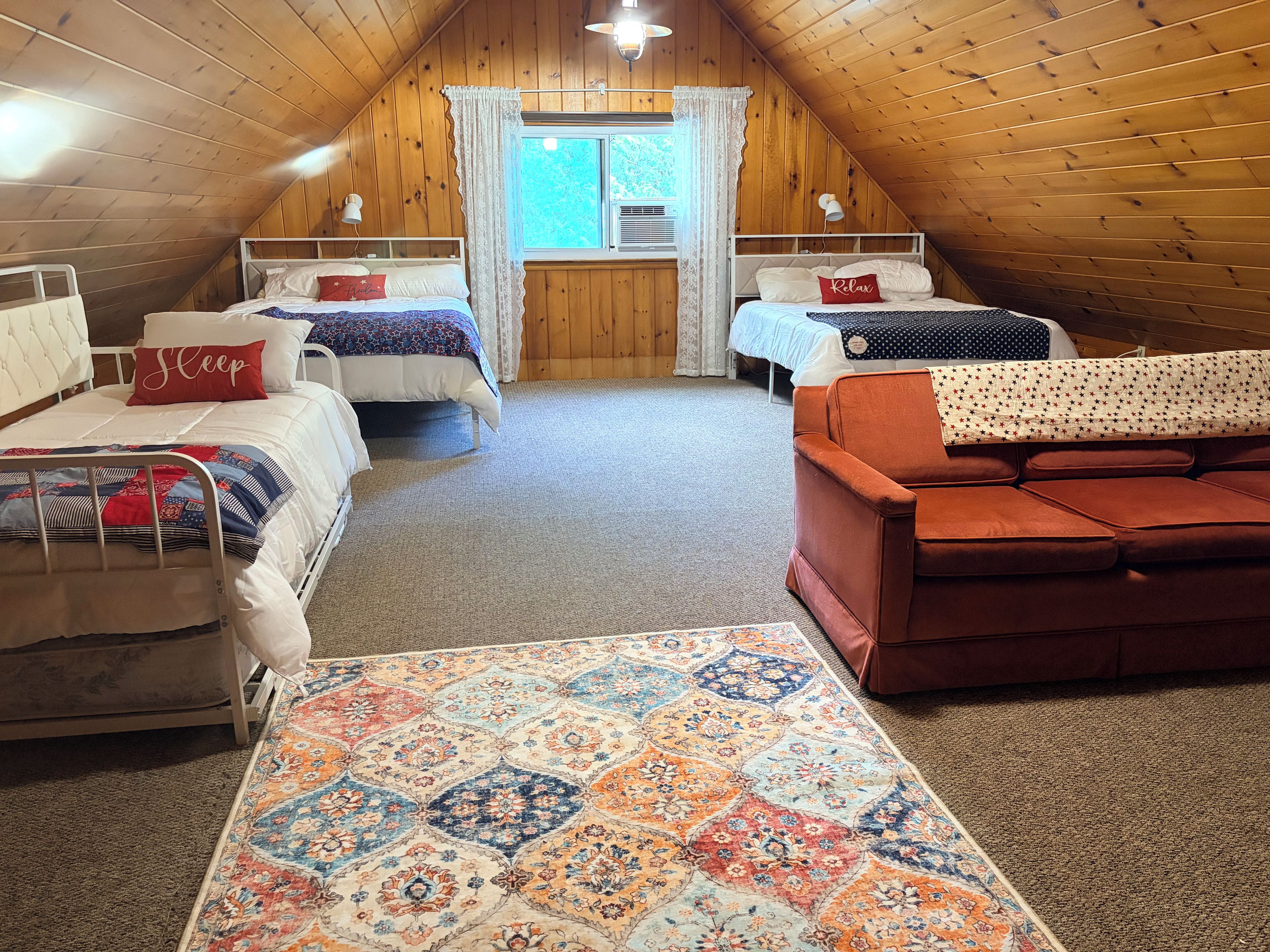 Une chambre mansardée chaleureuse, avec deux lits, un canapé et un tapis à motifs.