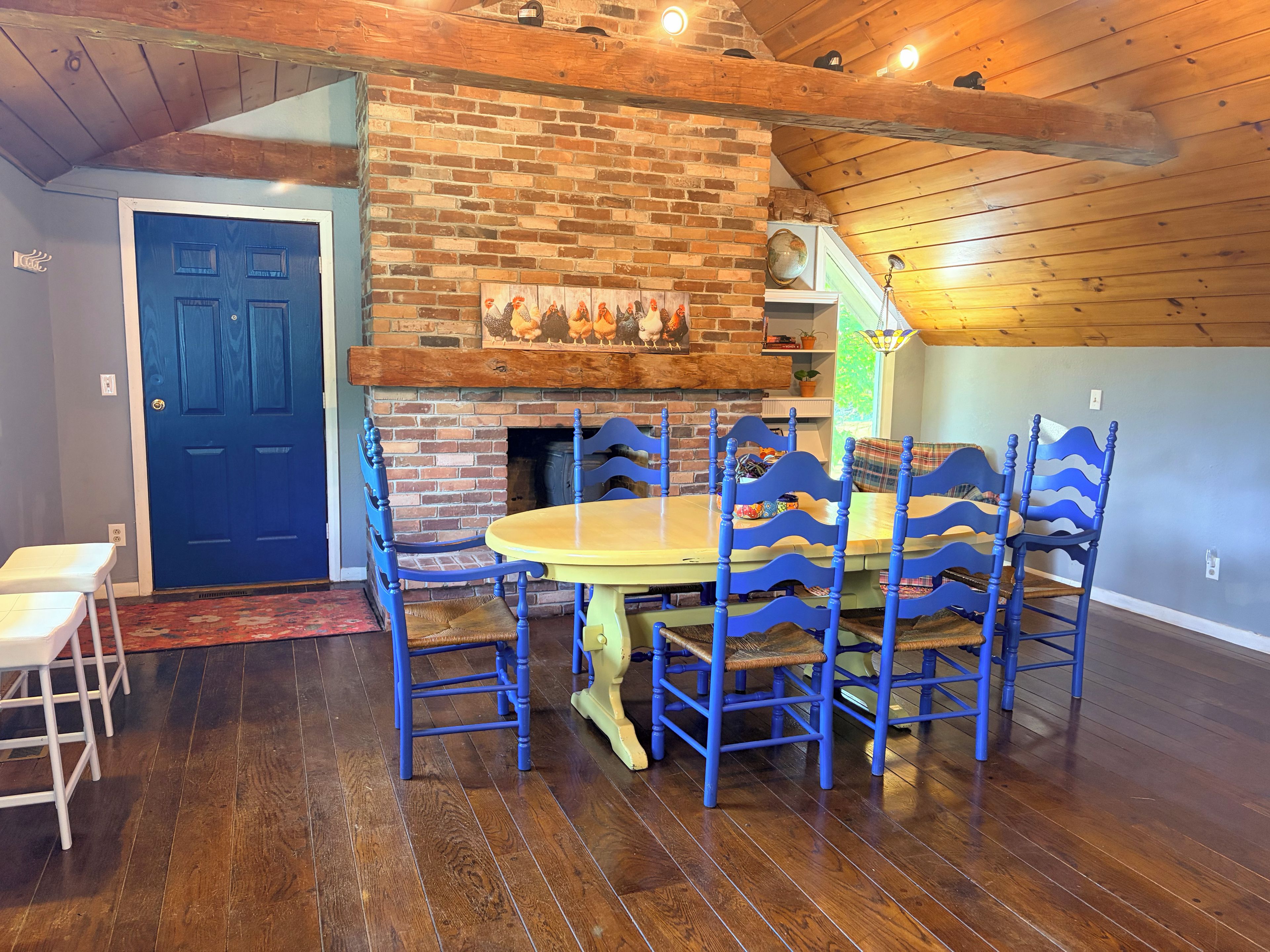 A dining area with a brick fireplace, blue chairs, and a wooden table.