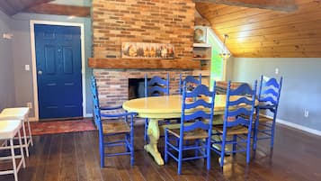 A dining area with a brick fireplace, blue chairs, and a wooden table.