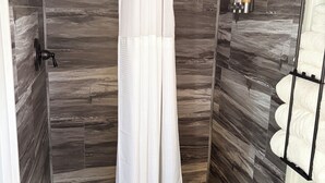 Une douche avec un rideau blanc, une pomme de douche à main et un luminaire fixé au mur.