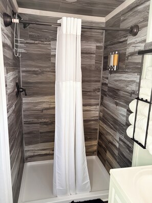 Eine Dusche mit weißer Duschvorhang, einer Handbrause und einer Wandleuchte.