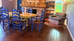 Un coin repas avec une cheminée en briques, des chaises bleues et un canapé à carreaux.