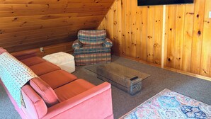 Une pièce chaleureuse avec un canapé rouge, un fauteuil à motifs et un téléviseur à écran plat fixé à un mur en bois.