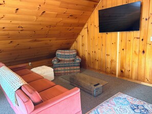 Ein gemütliches Zimmer mit einem roten Sofa, einem karierten Sessel und einem Flachbildfernseher, der an einer Holzwand befestigt ist.