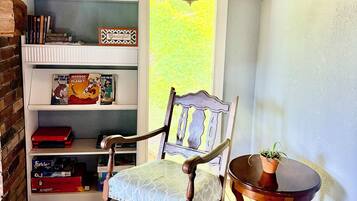 A cozy reading nook with a wooden chair, a small table, and a bookshelf filled with books.