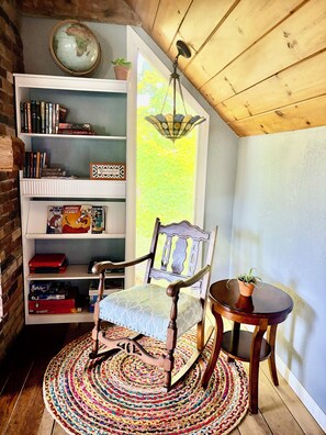 Un coin lecture confortable avec un fauteuil en bois, une petite table et une bibliothèque remplie de livres.