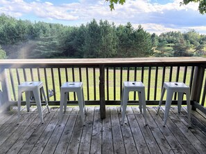 A wooden deck with three white plastic stools and a view of a grassy field and trees in the background. - The Upper Room: quiet, spacious guesthouse above a carriage barn in Harrisville (Harrisville)