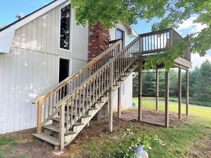 Un escalier en bois mène à un espace extérieur abrité, doté d’une cheminée en briques et d’une porte bleue.