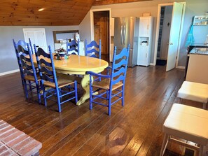 A dining area with a wooden table and blue chairs, a kitchen with a stainless steel refrigerator, and a white cabinet with a towel rack.