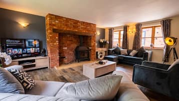A cozy living room with a brick fireplace, a flat-screen TV, comfortable seating, and a large window with curtains.