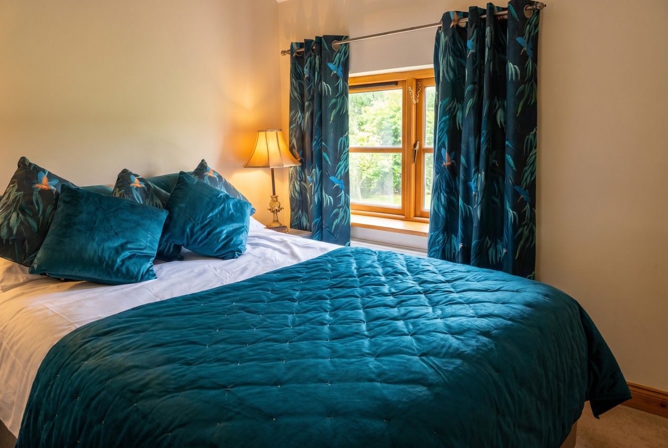 Un lit avec une couette et des oreillers de couleur turquoise, une lampe de chevet et une fenêtre avec des rideaux.