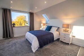 Een slaapkamer met een bed, nachtkastje, lamp, raam met gordijnen en een dakraam.