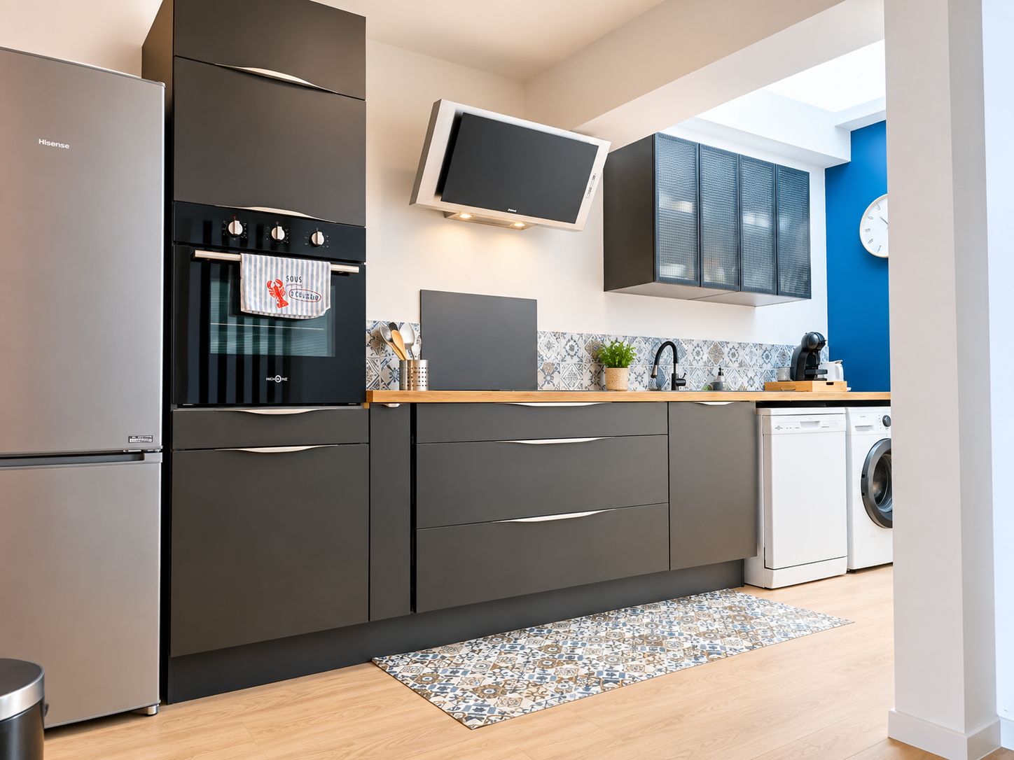 A modern kitchen with a built-in oven, a washing machine, and a flat-screen TV.