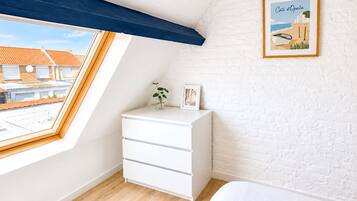 Een slaapkamer met dakraam, een witte dressoir, een bed en een ingelijst schilderij aan de muur.