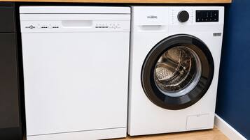 Un lave-linge et un sèche-linge à chargement frontal, dotés d’un panneau de commande, sont placés contre un mur bleu et au-dessus d’un plan de travail en bois.
