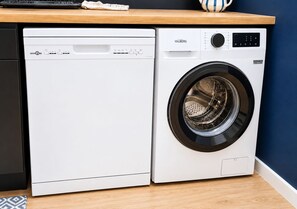 Un lave-linge et un sèche-linge à chargement frontal, dotés d’un panneau de commande, sont placés contre un mur bleu et au-dessus d’un plan de travail en bois.