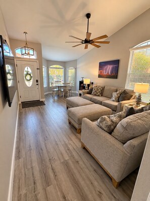 A spacious living room with a high ceiling, a ceiling fan, and a dining area with a table and chairs.