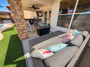 A covered outdoor seating area with a stone pillar, a table, and a sofa with cushions.