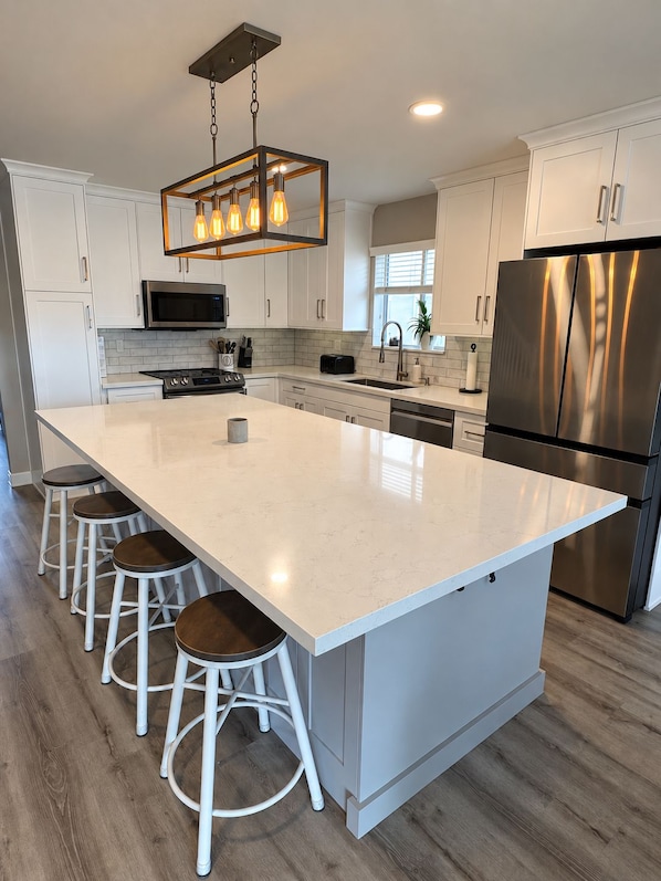 A modern kitchen with a large island, stainless steel appliances, and a hanging light fixture.
