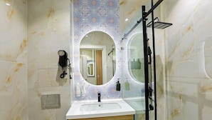 Casa de banho com toucador em mármore, cabine de duche em vidro e painel de azulejos decorativos.