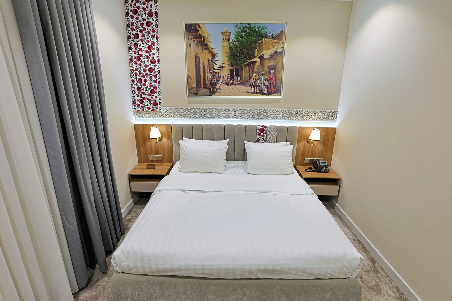 A hotel room with a large bed, two bedside tables with lamps, a decorative wall hanging, and a painting above the bed.