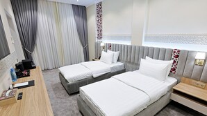 Quarto de hotel com duas camas, uma escrivaninha, uma cadeira, mesa de cabeceira e banheiro.