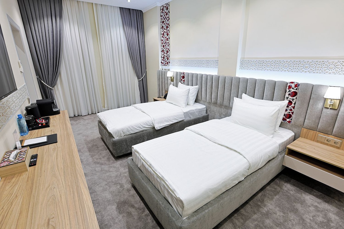 A hotel room with two beds, a desk, a chair, a nightstand, and a bathroom.