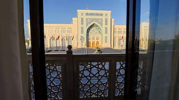 A view of a building with a large archway and multiple flags, viewed through a window with a lattice design.