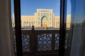 A view of a building with a large archway and multiple flags, viewed through a window with a lattice design. - Silk Way Hotel Tashkent by HMG (Tashkent)