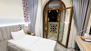 Quarto de hotel com uma cama, telefone de apoio, escrivaninha com computador e vista através de uma porta de vidro.