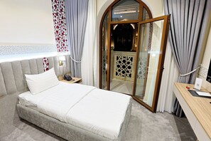 A hotel room with a bed, a bedside telephone, a desk with a computer, and a view through a glass door. - Silk Way Hotel Tashkent by HMG (Tashkent)