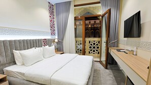 Quarto de hotel com uma cama grande, escrivaninha, televisão e vista para um edifício através de uma porta de vidro.