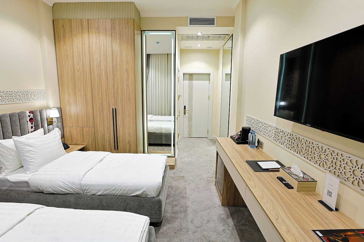 A hotel room with two beds, a desk, a TV, and a wardrobe.