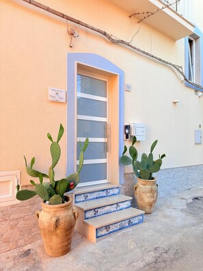 A building with a blue-framed door, numbered 10, and two potted cacti on the steps.