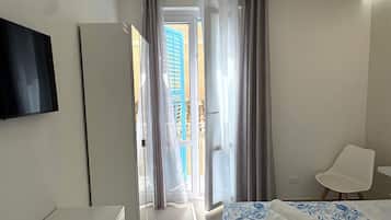 A hotel room with a bed, a TV, a chair, and a view of the outside.