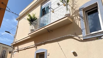 Ein zweistöckiges Gebäude mit Balkon, einer Tür und einem kleinen Garten mit Pflanzen.