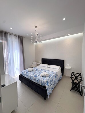A modern bedroom with a large bed, a chandelier, and a white wall with a leaf pattern. - U SULI DO MARI, RELAIS SUL MARE Apartment in the heart of Pozzallo. (Pozzallo)