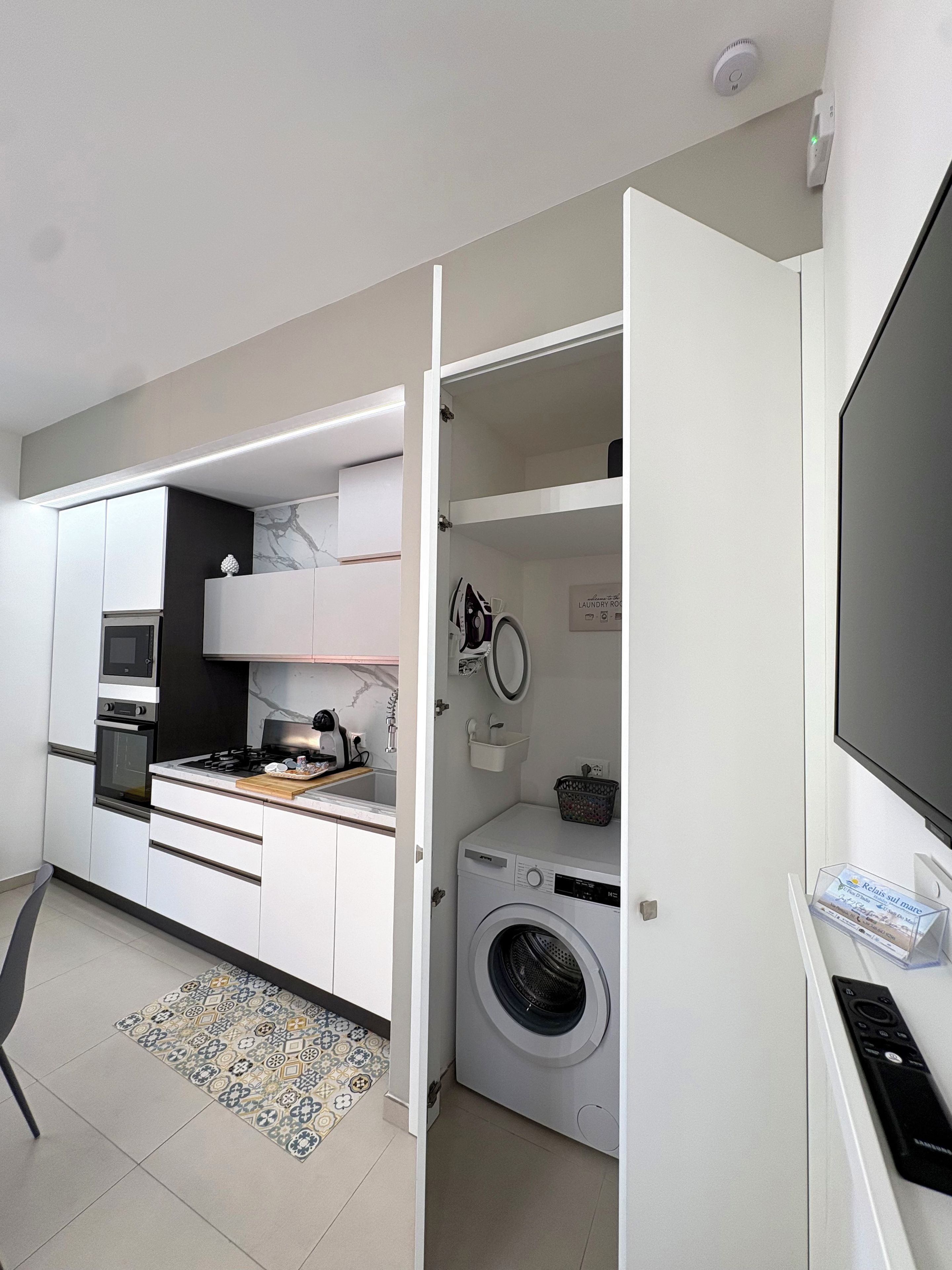 A compact kitchen with built-in appliances, a washing machine, and a flat-screen TV.